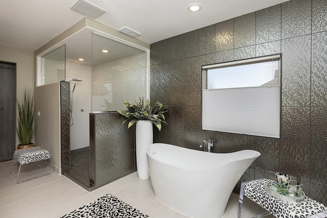 bathroom featuring tile patterned flooring, visible vents, a walk in shower, tile walls, and a soaking tub