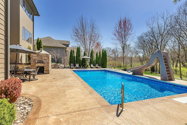 view of swimming pool with a patio area, an outdoor stone fireplace, a water slide, and a fenced in pool