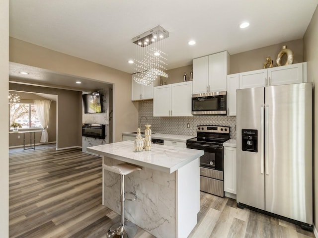 1710 Forest Ave, Des Moines, IA 50314 - kitchen with white cabinets, stainless steel appliances, light wood-type flooring, backsplash, and light stone counters