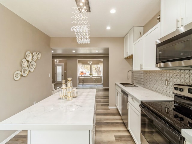 1710 Forest Ave, Des Moines, IA 50314 - kitchen featuring light wood finished floors, a sink, backsplash, a notable chandelier, and appliances with stainless steel finishes