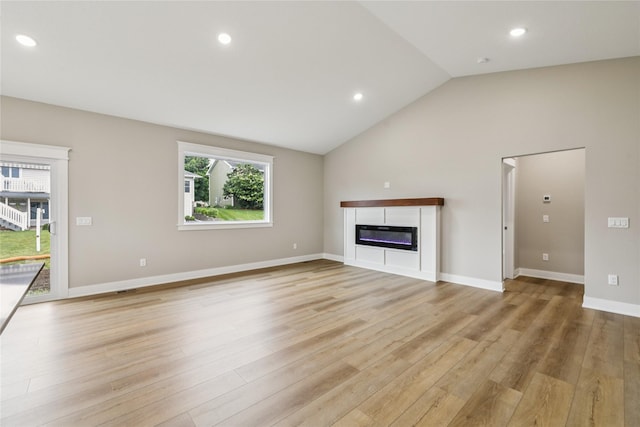 2311 N 8th Ave E, Newton, IA 50208 - unfurnished living room featuring light wood finished floors, vaulted ceiling, a glass covered fireplace, and recessed lighting