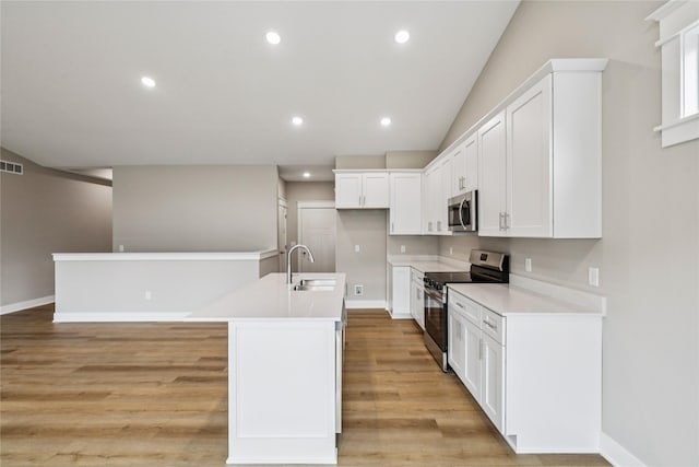 2311 N 8th Ave E, Newton, IA 50208 - kitchen featuring stainless steel appliances, a kitchen island with sink, light wood-style floors, white cabinetry, and light countertops