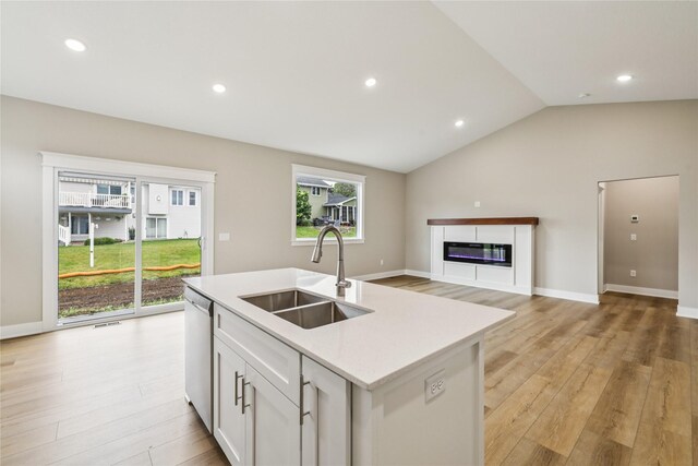 2311 N 8th Ave E, Newton, IA 50208 - kitchen featuring dishwasher, light countertops, light wood-style flooring, an island with sink, and a glass covered fireplace