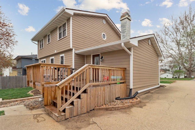 rear view of house featuring a chimney, fence, and a deck