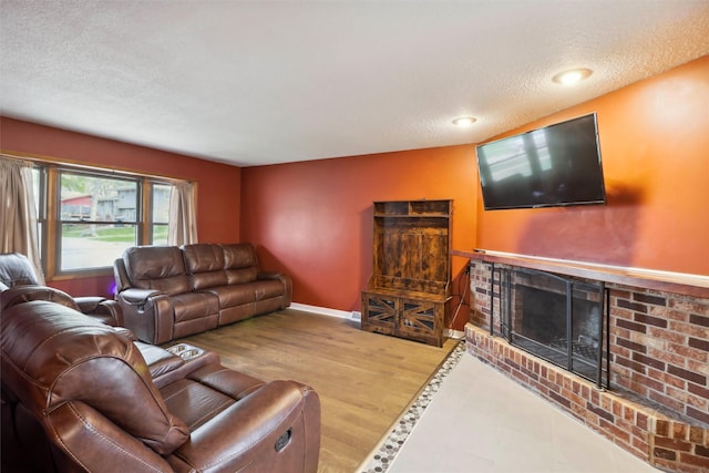 living room featuring a textured ceiling, wood finished floors, a brick fireplace, and baseboards