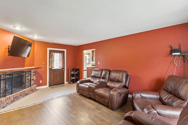 living room featuring baseboards, hardwood / wood-style floors, a textured ceiling, and a fireplace