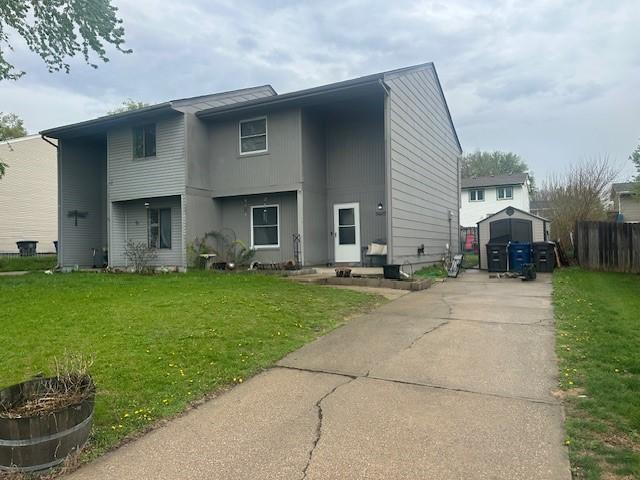 rear view of house featuring an outbuilding, concrete driveway, and a lawn