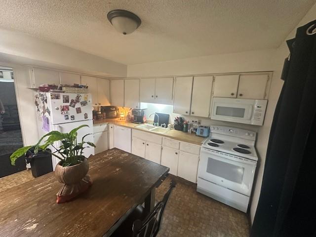 kitchen featuring a sink, white appliances, white cabinetry, light countertops, and a textured ceiling