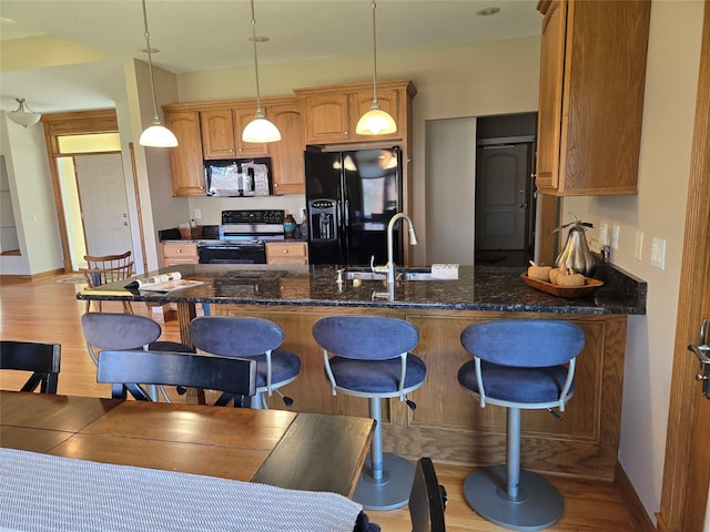 kitchen with a kitchen bar, black appliances, a sink, and light wood finished floors