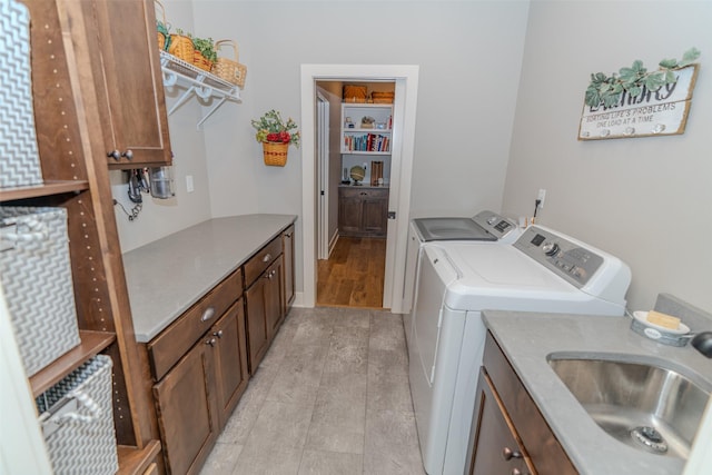washroom featuring cabinet space, light wood-style flooring, washer and clothes dryer, and a sink