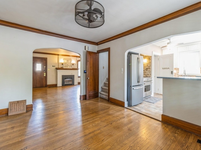3826 Grand Ave, Des Moines, IA 50312 - unfurnished living room featuring a ceiling fan, arched walkways, a brick fireplace, light wood-type flooring, and ornamental molding