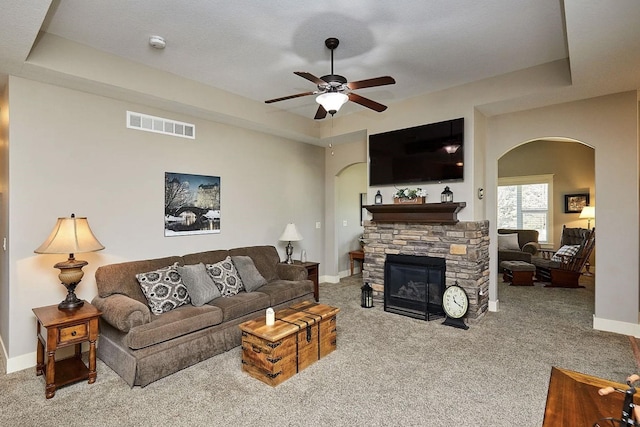 living area with carpet, a raised ceiling, visible vents, arched walkways, and ceiling fan