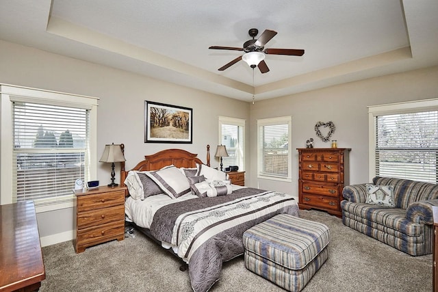 carpeted bedroom featuring a tray ceiling and a ceiling fan