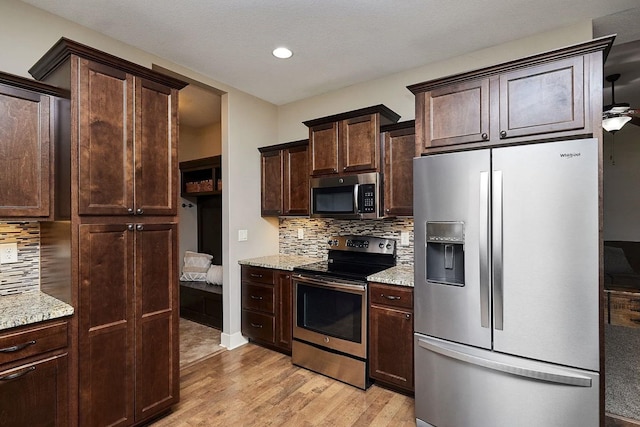 kitchen featuring dark brown cabinets, decorative backsplash, light wood-style floors, stainless steel appliances, and light stone countertops