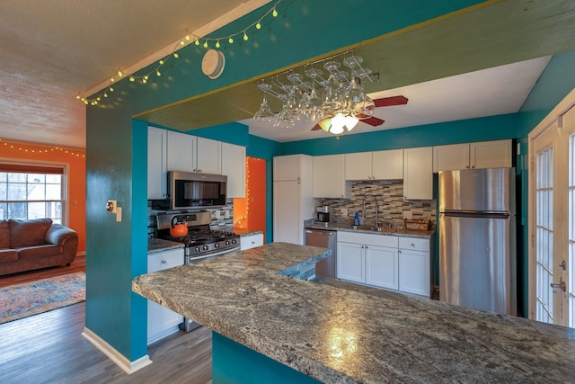 310 E Emma Ave, Des Moines, IA 50315 - kitchen with appliances with stainless steel finishes, wood finished floors, white cabinetry, decorative backsplash, and a textured ceiling