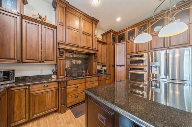 9289 Winterberry Ct, West Des Moines, IA 50266 - kitchen with dark stone countertops, brown cabinets, stainless steel appliances, light wood finished floors, and backsplash