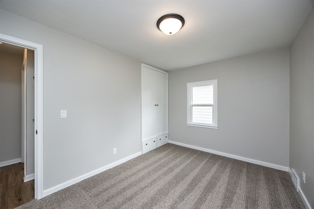 spare room with visible vents, dark colored carpet, and baseboards