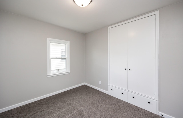 unfurnished bedroom with dark colored carpet, a closet, and baseboards