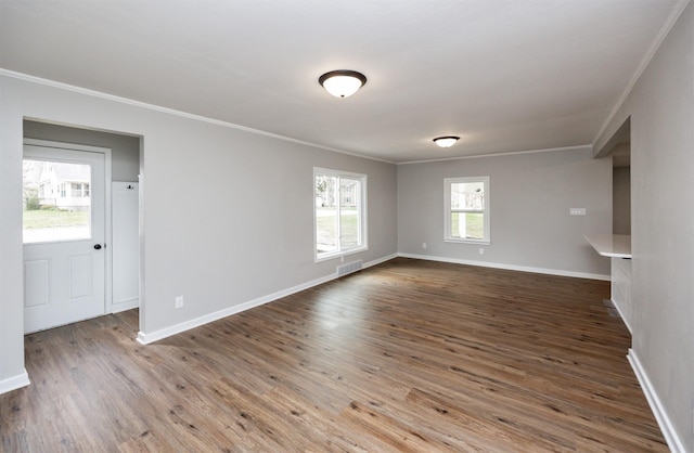 empty room with wood finished floors, visible vents, crown molding, and baseboards