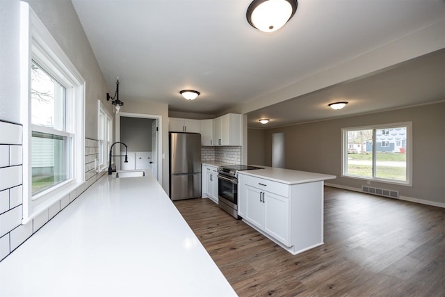kitchen with a peninsula, a sink, visible vents, backsplash, and appliances with stainless steel finishes