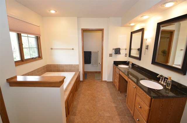 full bathroom with a tub to relax in, double vanity, baseboards, and a sink
