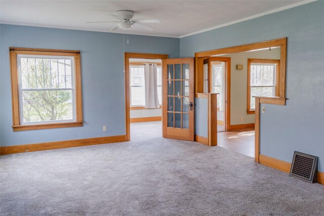 carpeted empty room featuring french doors, baseboards, visible vents, ceiling fan, and ornamental molding