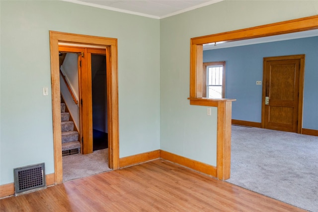 carpeted empty room with baseboards, visible vents, wood finished floors, stairway, and ornamental molding