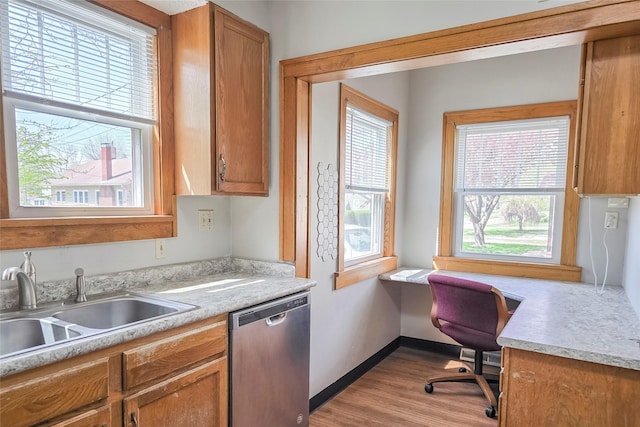 kitchen featuring stainless steel dishwasher, light wood-style flooring, a sink, brown cabinetry, and light countertops