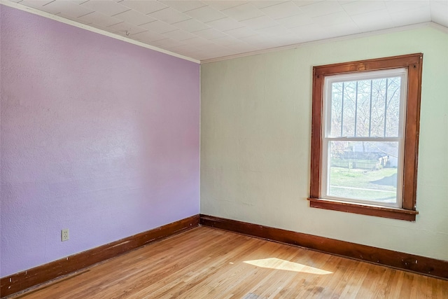 empty room featuring light wood-style flooring, baseboards, and crown molding