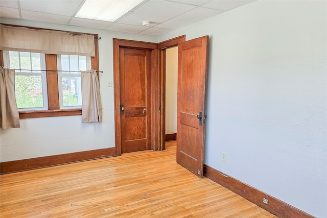 spare room with a paneled ceiling, light wood finished floors, and baseboards