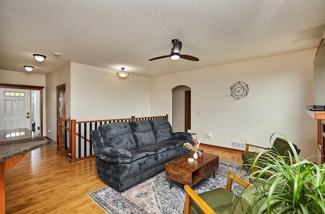 living room featuring arched walkways, a ceiling fan, visible vents, and light wood-style flooring