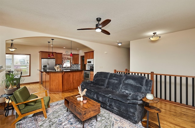 living room with arched walkways, light wood finished floors, baseboards, and ceiling fan