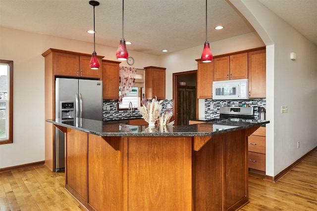 kitchen with tasteful backsplash, appliances with stainless steel finishes, brown cabinetry, and light wood-style flooring