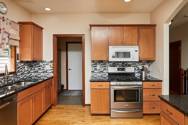 kitchen featuring light wood finished floors, a sink, dark stone countertops, decorative backsplash, and appliances with stainless steel finishes