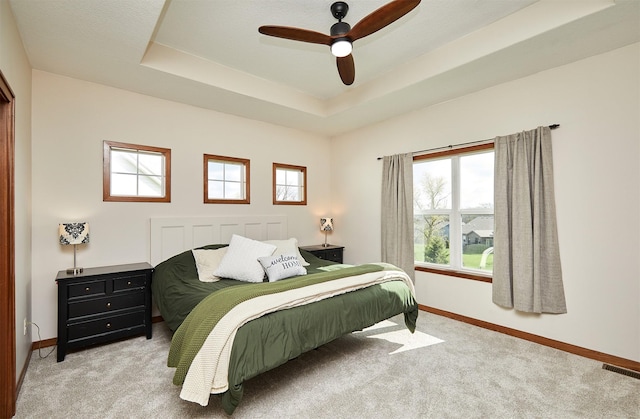 carpeted bedroom with a tray ceiling, visible vents, a ceiling fan, and baseboards