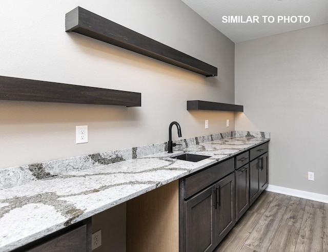 bar with baseboards, a sink, and light wood finished floors