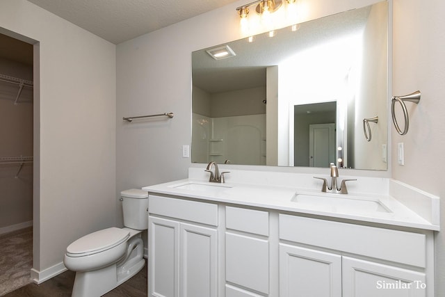 bathroom featuring a walk in closet, double vanity, toilet, and a sink
