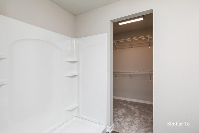 bathroom featuring walk in shower, a spacious closet, and baseboards