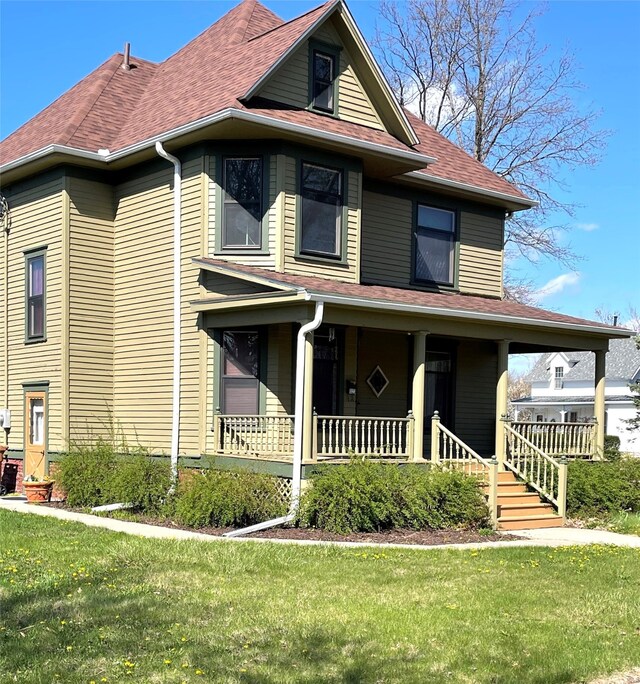 view of front of property featuring a porch, roof with shingles, and a front yard