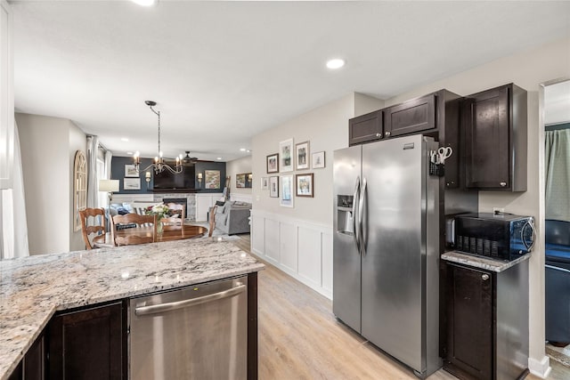 kitchen featuring light stone counters, wainscoting, open floor plan, stainless steel appliances, and light wood-style flooring