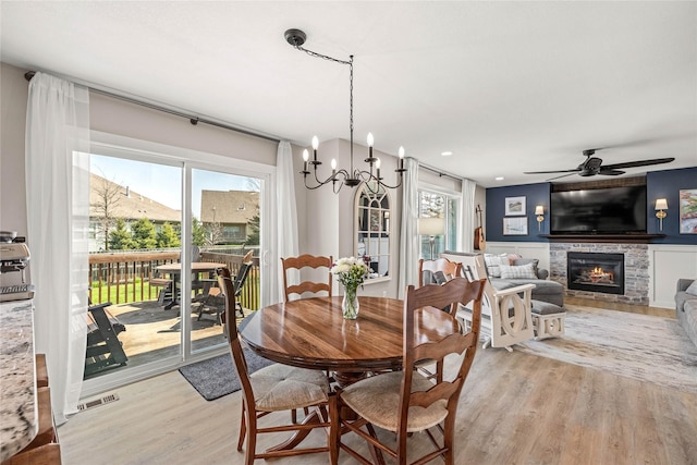 dining space with a glass covered fireplace, light wood-type flooring, visible vents, and ceiling fan with notable chandelier