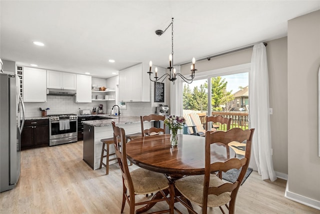 dining area with light wood-type flooring, baseboards, recessed lighting, and a notable chandelier