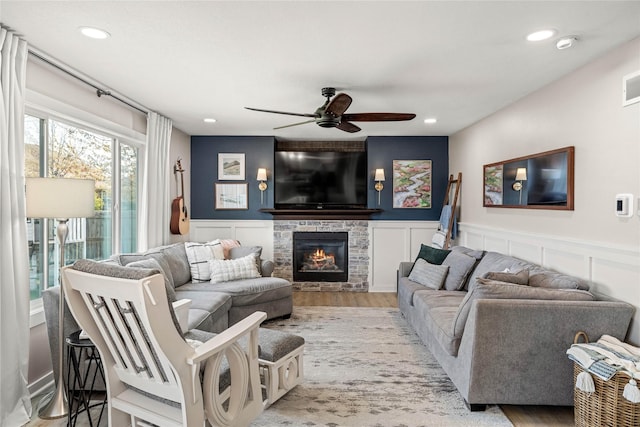 living area featuring a decorative wall, a ceiling fan, a stone fireplace, and recessed lighting