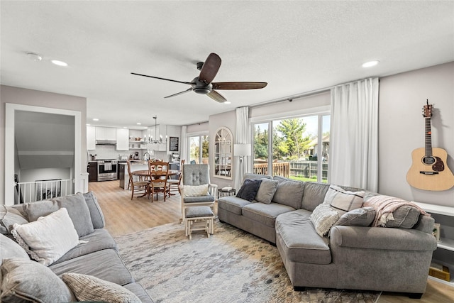 living area with recessed lighting, light wood finished floors, and ceiling fan with notable chandelier