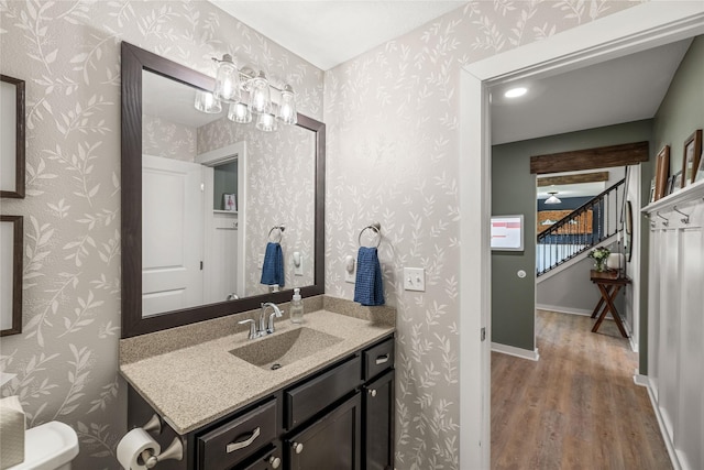 bathroom featuring baseboards, vanity, wood finished floors, and wallpapered walls