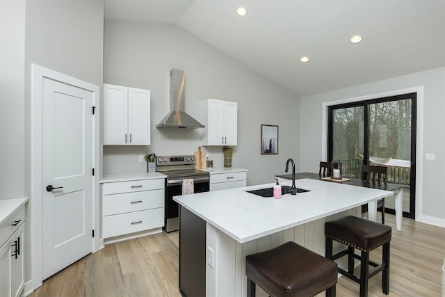 1040 W Trace Pl, Polk City, IA 50226 - kitchen with stainless steel range with electric cooktop, wall chimney range hood, a sink, light wood-type flooring, and a kitchen island with sink