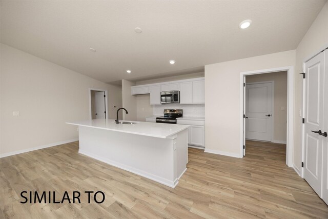 16514 Ironwood Ln, Urbandale, IA 50323 - kitchen with stainless steel appliances, a sink, white cabinetry, a kitchen island with sink, and light wood-type flooring