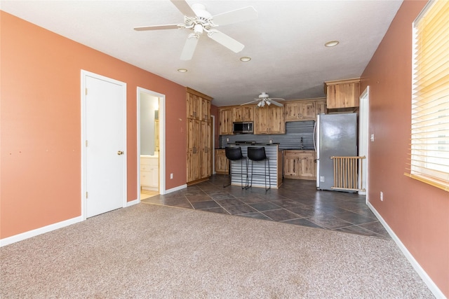 kitchen featuring brown cabinetry, ceiling fan, dark colored carpet, and appliances with stainless steel finishes