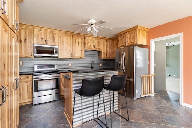 kitchen featuring stainless steel appliances, a breakfast bar area, decorative backsplash, a ceiling fan, and dark countertops