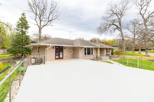 view of front of property with fence, french doors, concrete driveway, a chimney, and a shingled roof